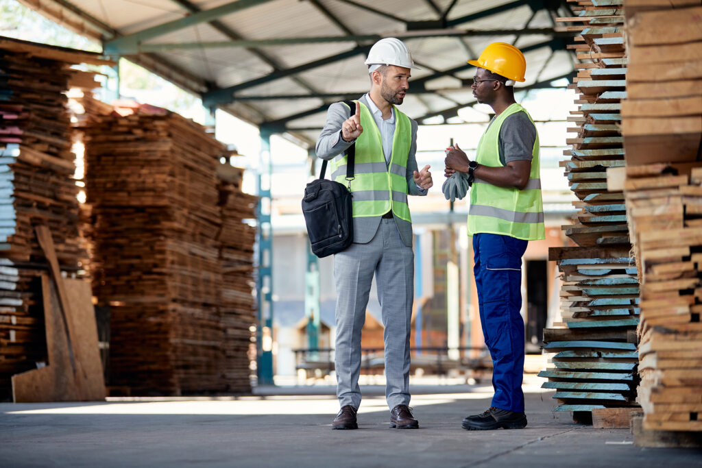 Warehouse inspector giving instructions to African American worker in lumber distribution department.